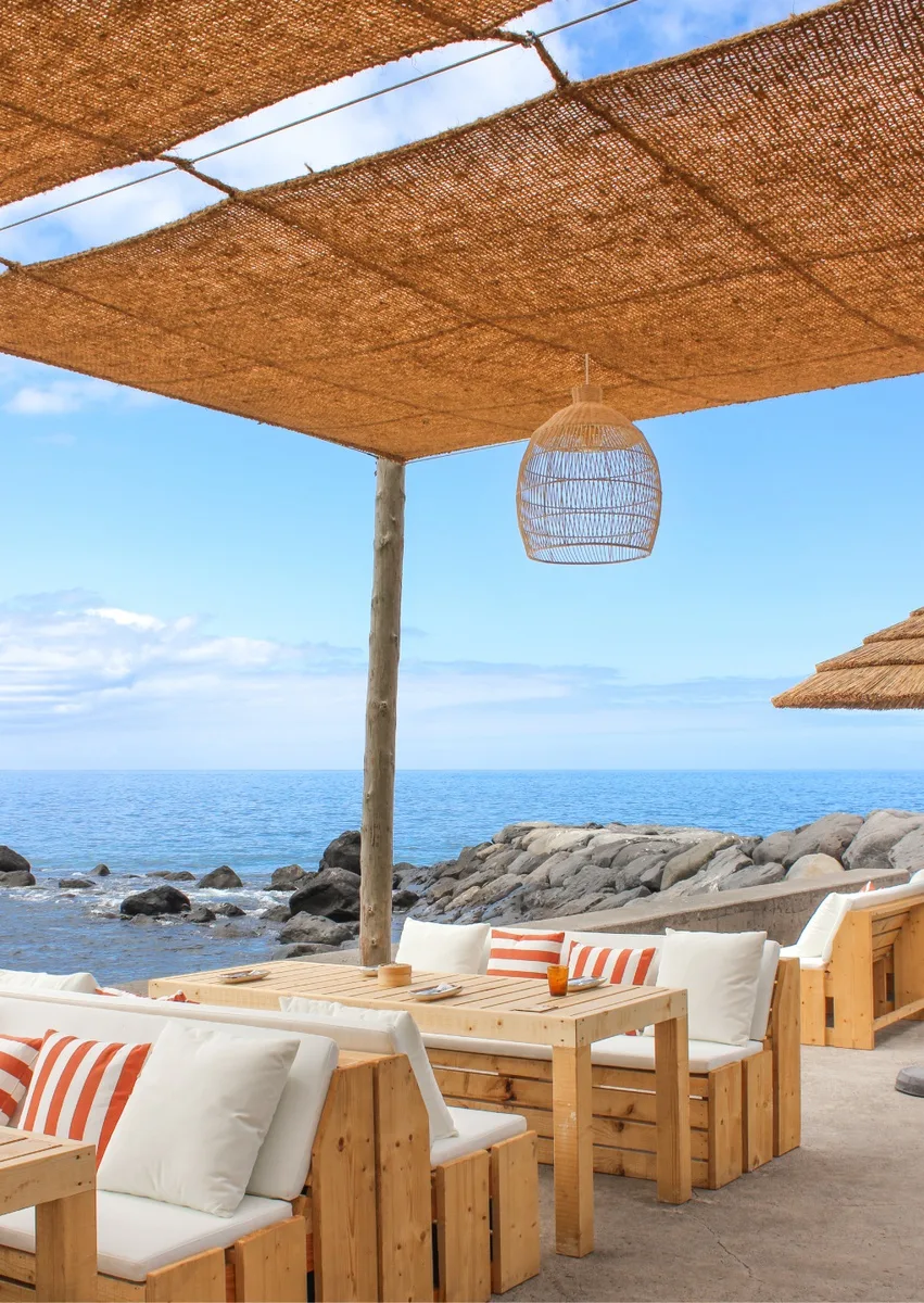 A beach bar near Praia da Calheta — wooden loungers under a reed canopy, looking out to the ocean
